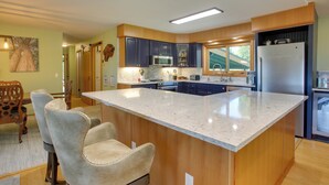 Una cocina con una isla grande, armarios de madera y un comedor con sillas.
