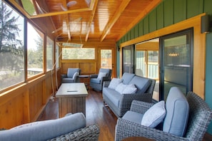 A wooden deck with wicker furniture, a table, and large windows.