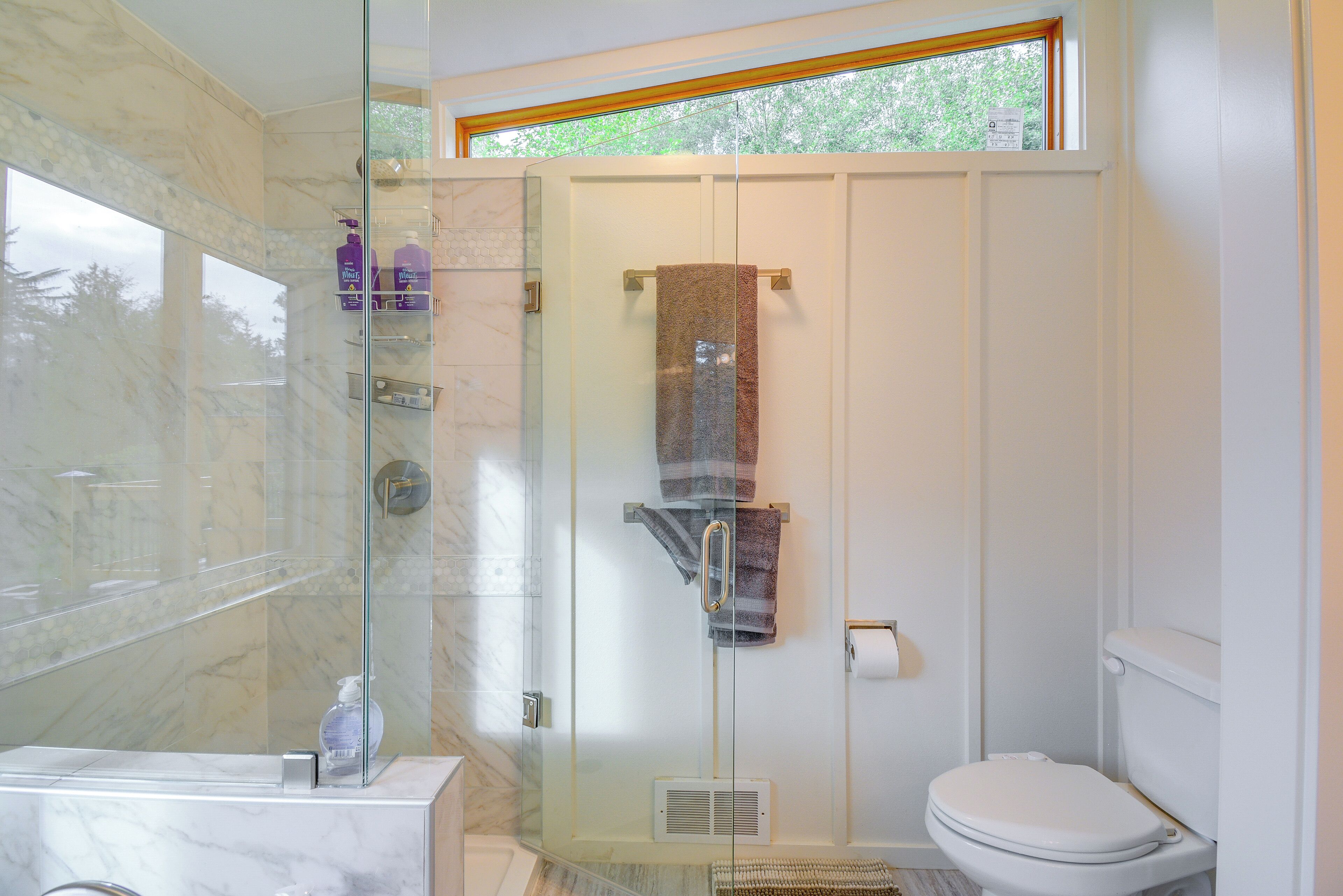 A modern bathroom with a glass-enclosed shower, a toilet, and a marble sink.