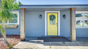 Une maison avec une porte d’entrée jaune, des colonnes en bois et un petit porche.