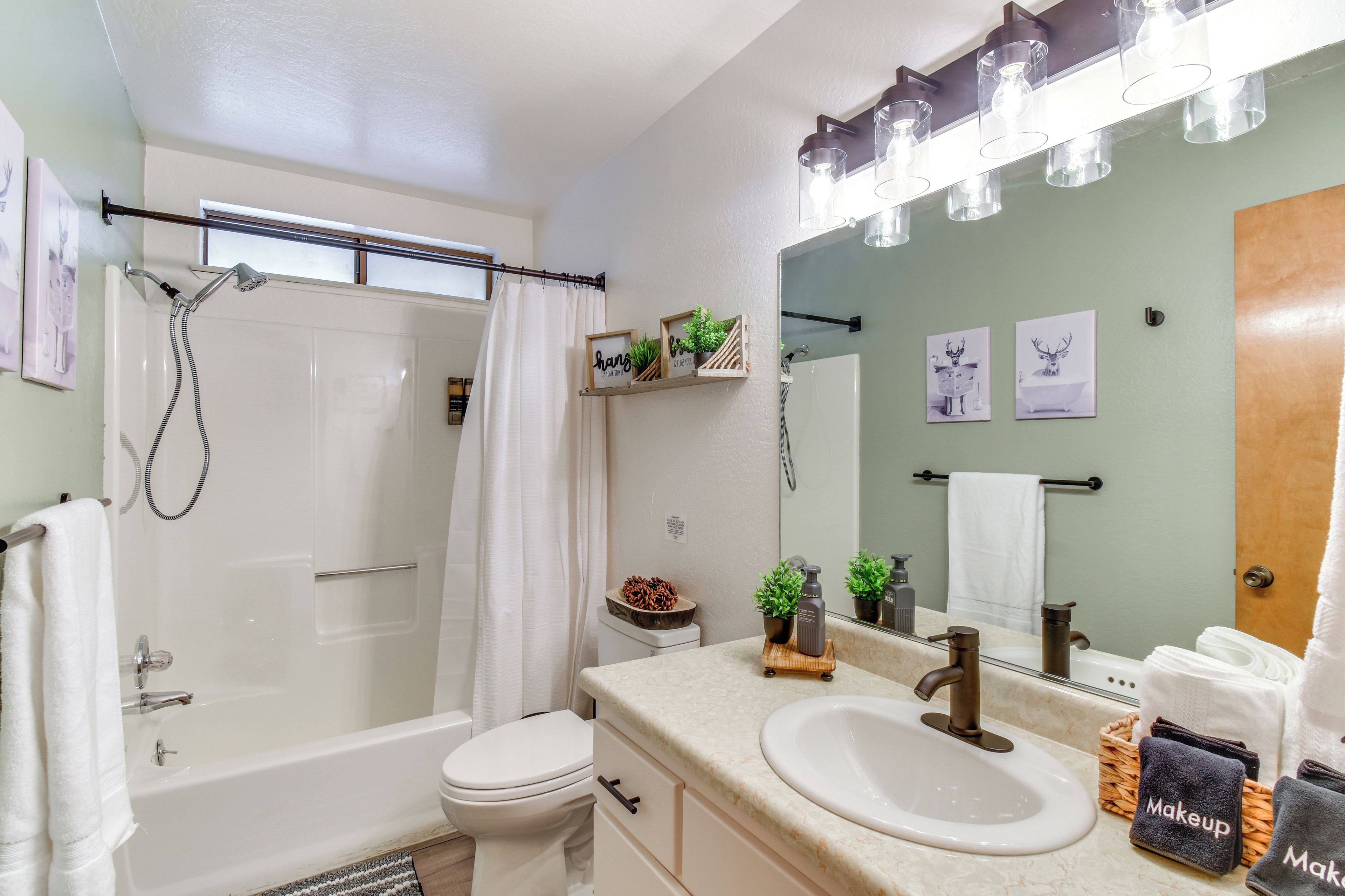 Un baño moderno con bañera, inodoro y dos lavamanos. Hay plantas decorativas y un espejo sobre los lavamanos.