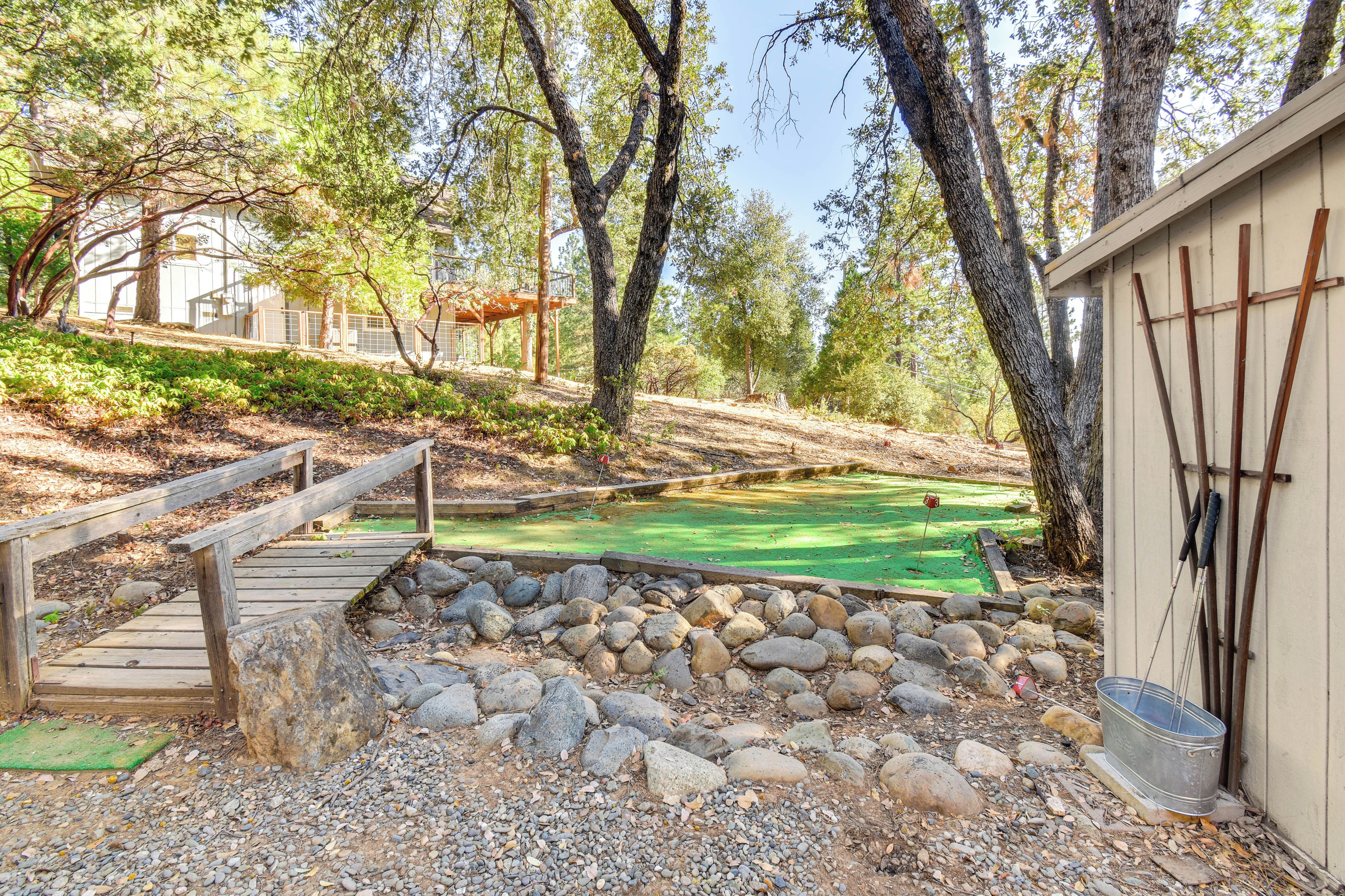A wooden bridge leading to a green-roofed building, surrounded by trees and rocks.
