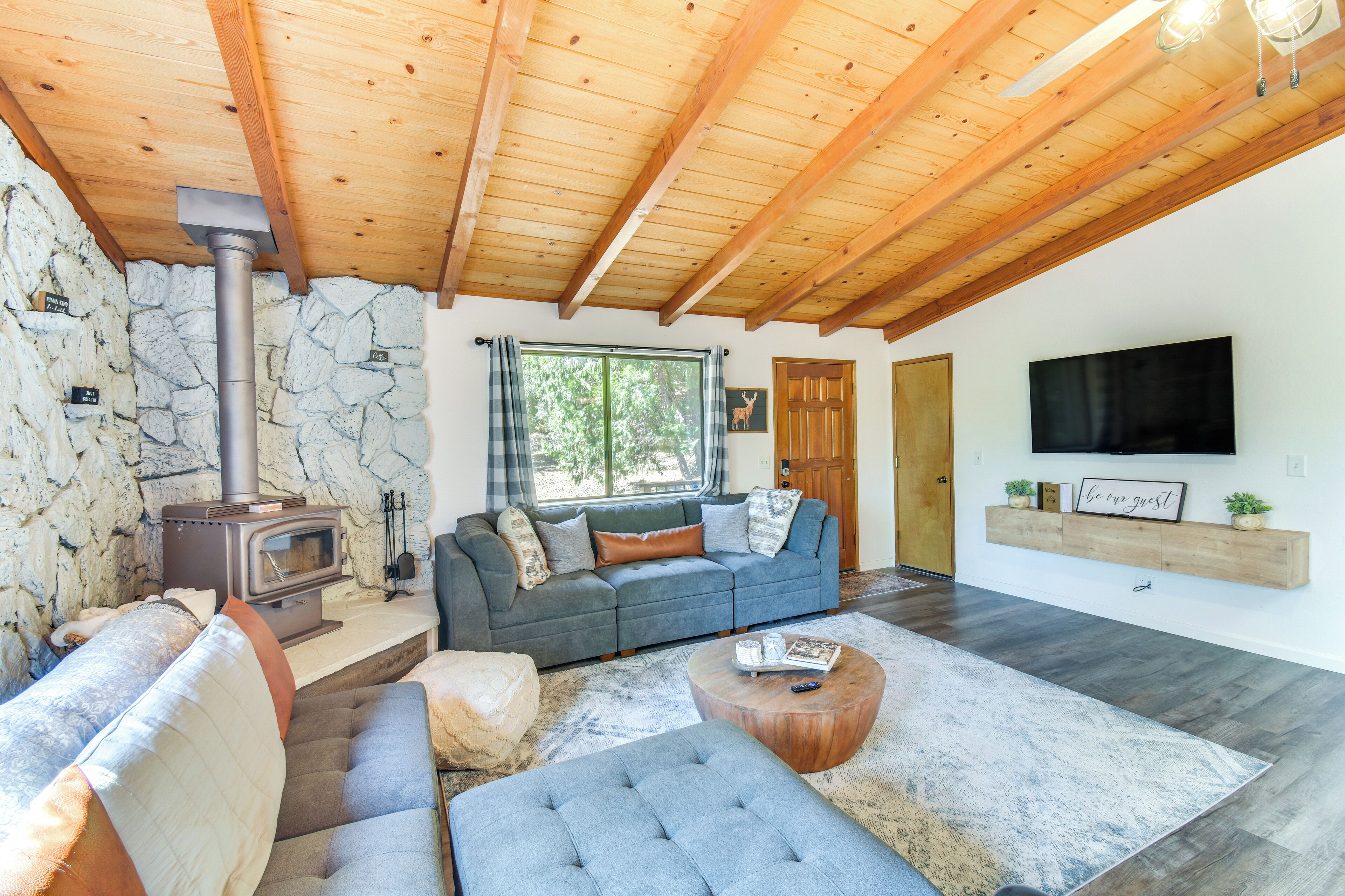 Ein gemütliches Wohnzimmer mit Steinwand, grauem Sofa, Holzboden und Kamin.