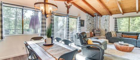 Amplia sala de estar con techo de madera, chimenea de piedra y grandes ventanales con vistas al exterior.