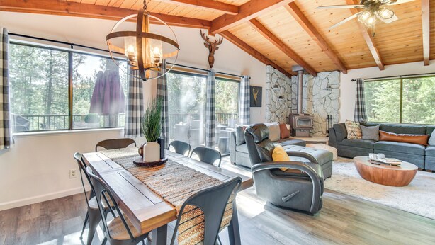 Un vaste espace de vie doté d’un plafond en bois, d’une cheminée en pierre et de grandes fenêtres offrant une vue sur l’extérieur.