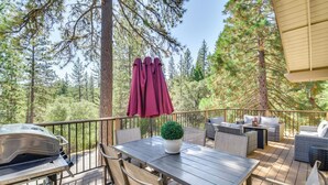 Une terrasse en bois, dotée de mobilier d’extérieur, d’un barbecue et offrant une vue sur une forêt.