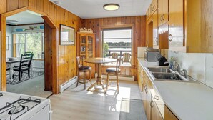 A wooden cabin kitchen with a dining table, chairs, a stove, and a large window overlooking a lake. - Waterfront Cottage w/ Dock & Views in Six Lakes! (Six Lakes)