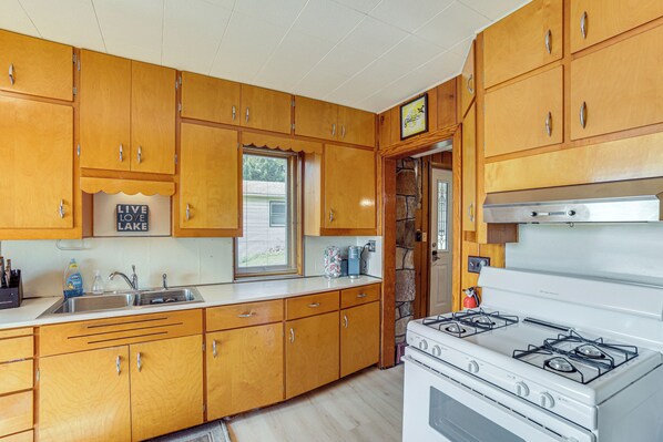 A kitchen with wooden cabinets, a white stove, and a window with blinds. - Waterfront Cottage w/ Dock & Views in Six Lakes! (Six Lakes)