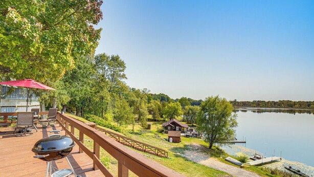 A wooden deck with a barbecue grill, outdoor furniture, and a view of a lake and dock. - Waterfront Cottage w/ Dock & Views in Six Lakes! (Six Lakes)