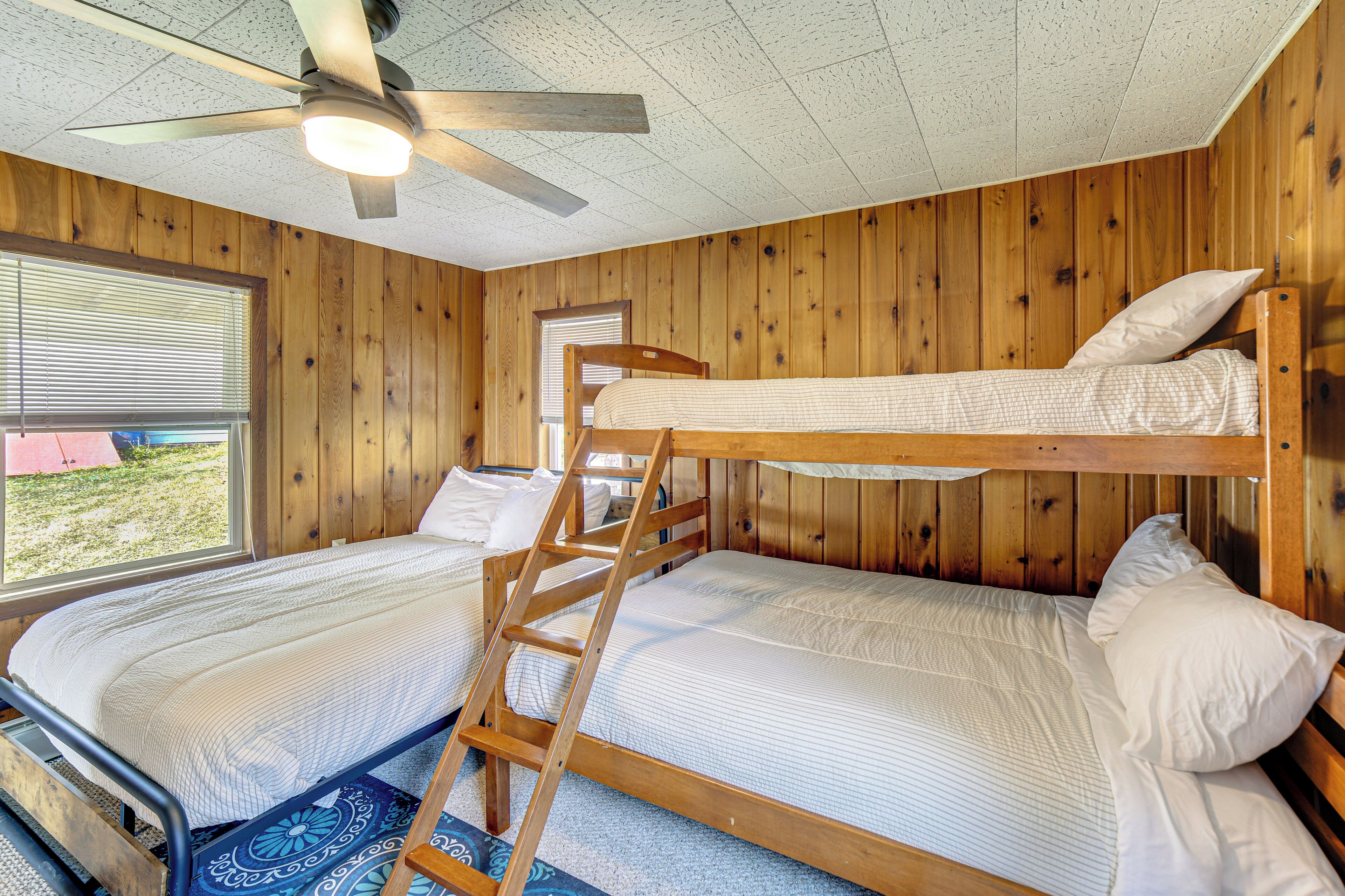 A room with two bunk beds, wooden walls, a ceiling fan, and a window with blinds.