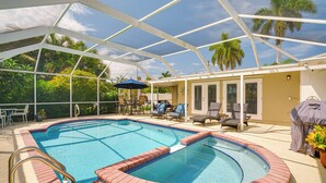 A covered outdoor swimming pool with a glass ceiling, surrounded by lounge chairs and a barbecue area. - Canal-front Home w/ Boat Lift in Cape Coral! (Cape Coral)