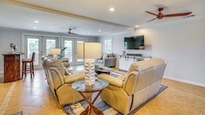 A spacious living room with a beige leather sofa, a glass coffee table, and a ceiling fan. - Canal-front Home w/ Boat Lift in Cape Coral! (Cape Coral)