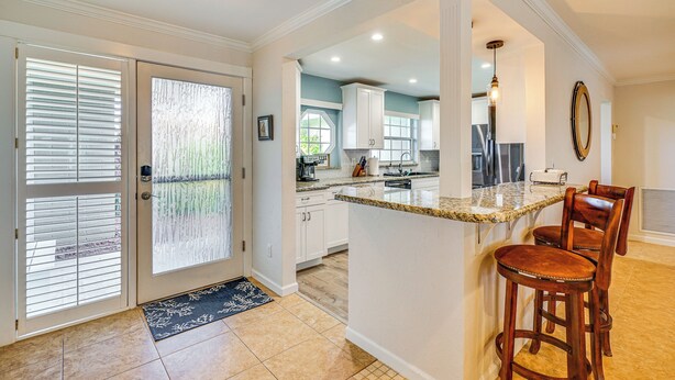 A kitchen with white cabinets, a granite countertop, and a bar area with stools. - Canal-front Home w/ Boat Lift in Cape Coral! (Cape Coral)