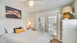 A bedroom with a bed, a ceiling fan, a nightstand with a lamp, a dresser, and a window with blinds. - Canal-front Home w/ Boat Lift in Cape Coral! (Cape Coral)
