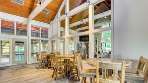 Un comedor amplio con mesas y sillas de madera, ventanas grandes y vistas a la vegetación exterior.