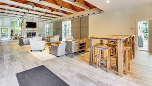 Un espacio habitable amplio con techo alto, vigas de madera, chimenea y un televisor grande montado en la pared.
