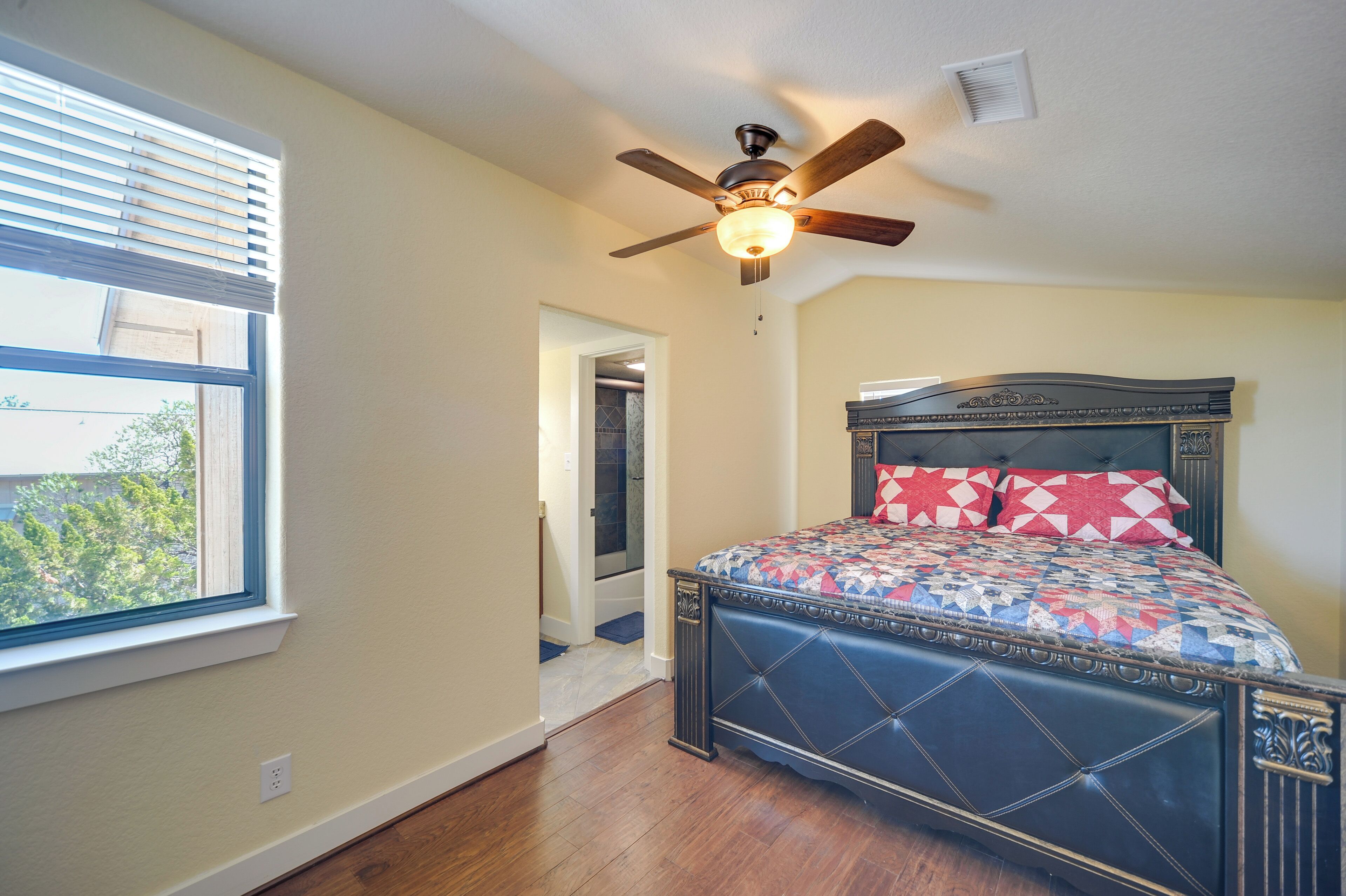 A bedroom with a bed, a ceiling fan, a window, and a door leading to another room.