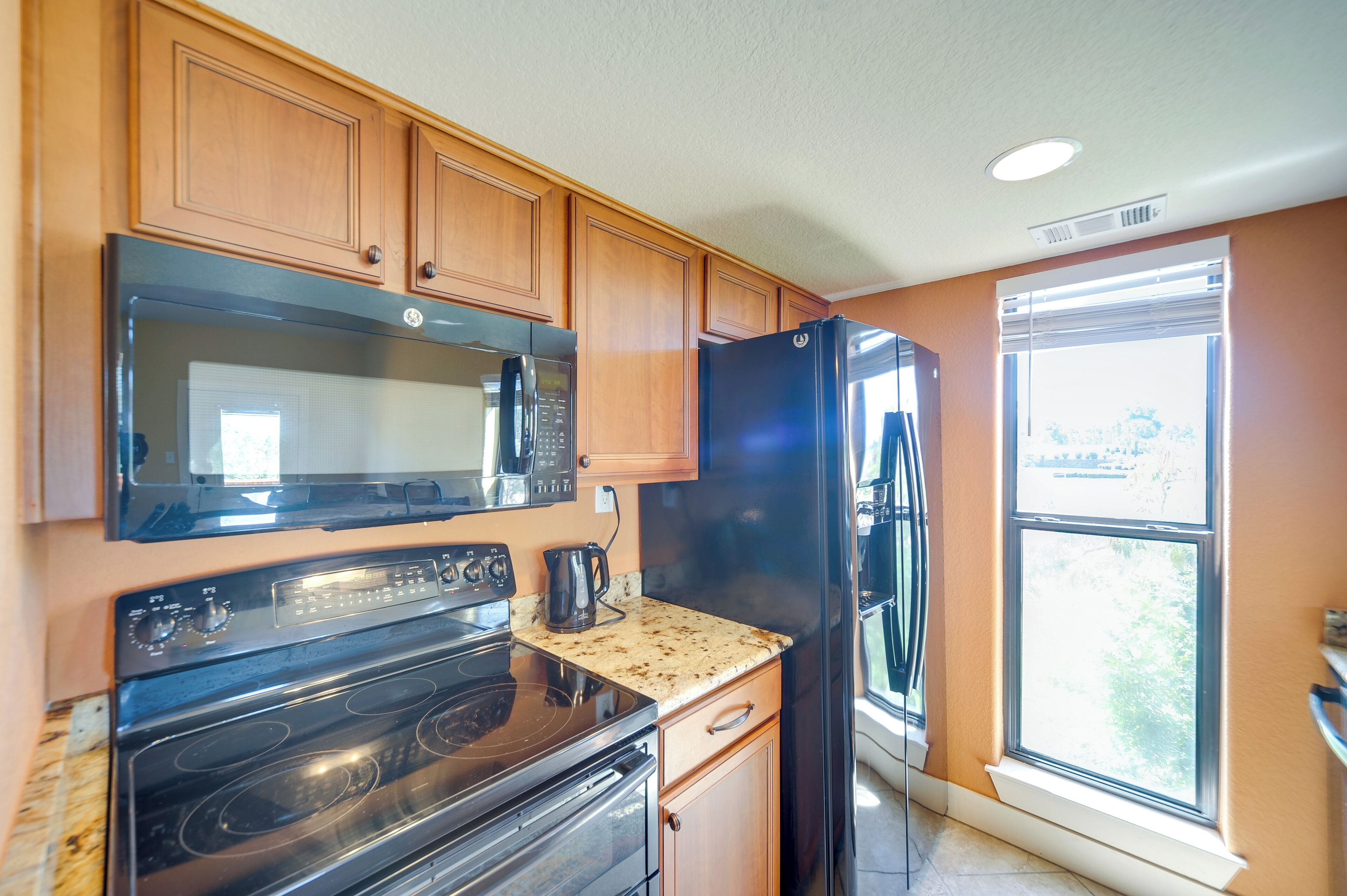 A kitchen with wooden cabinets, a black microwave, a black refrigerator, and a stove.