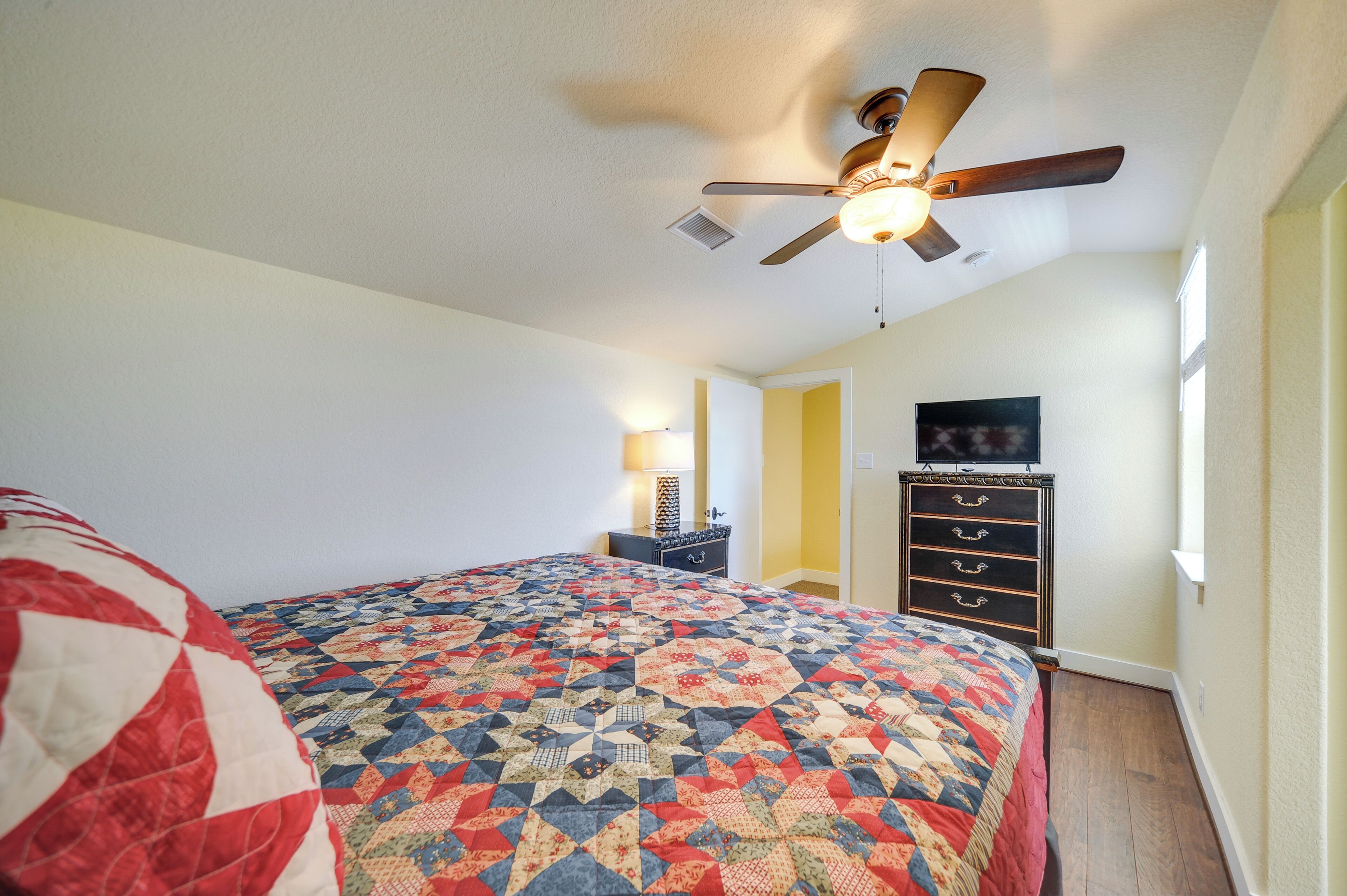 A bedroom with a bed, a ceiling fan, a dresser, and a TV.
