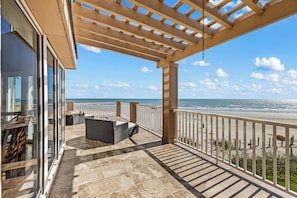 A covered outdoor area with a view of the beach, featuring a seating area and a pergola.