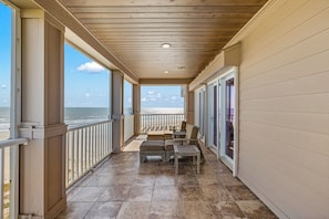 A covered balcony with a view of the ocean, featuring a seating area with a table and chairs.