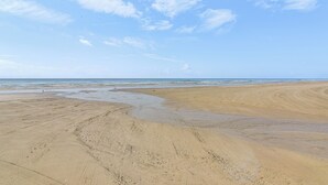 Ein weiter Sandstrand mit sanften Wellen und blauem Himmel.