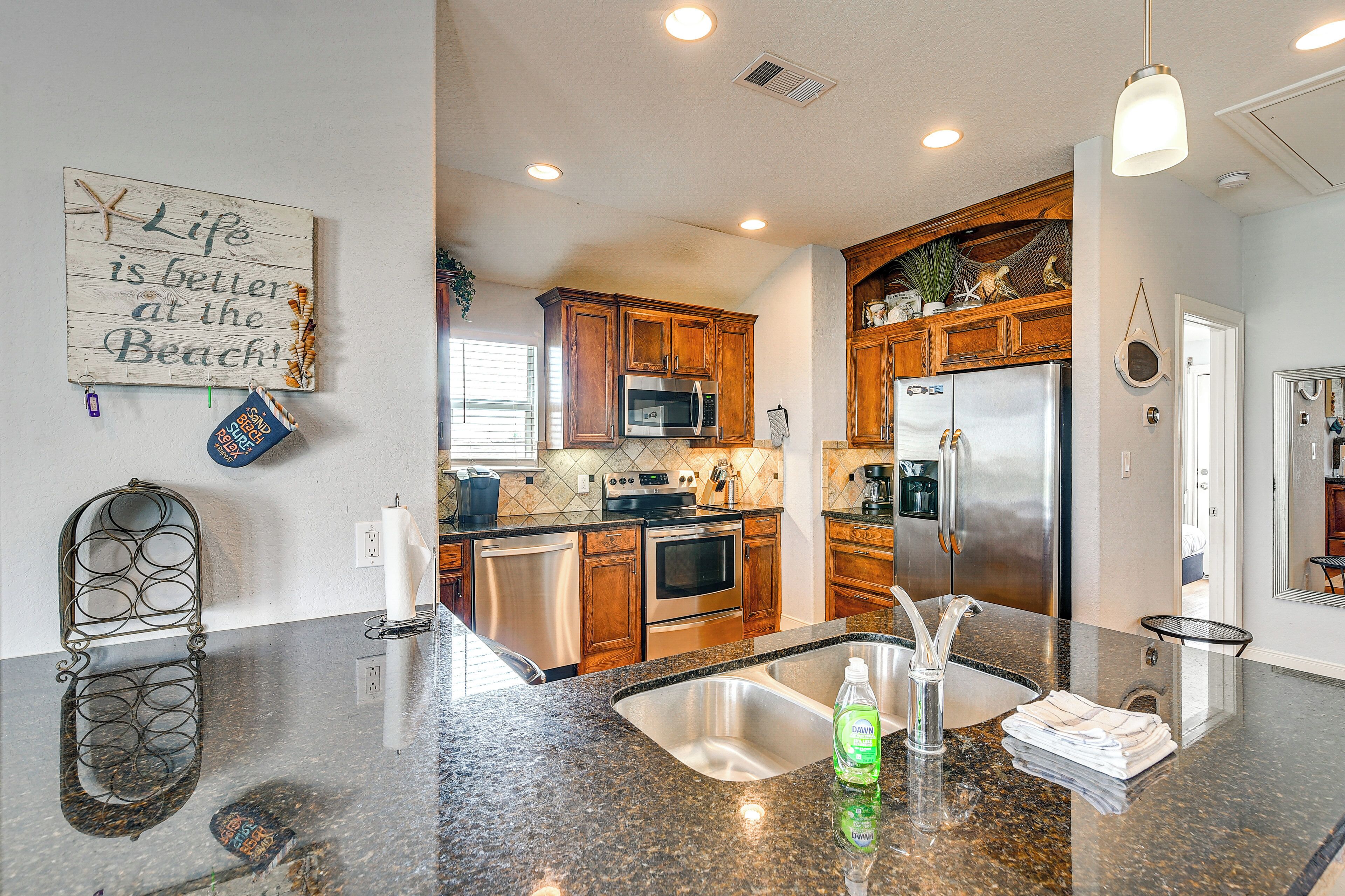 A kitchen with granite countertops, stainless steel appliances, wooden cabinets, and a beach-themed decor.