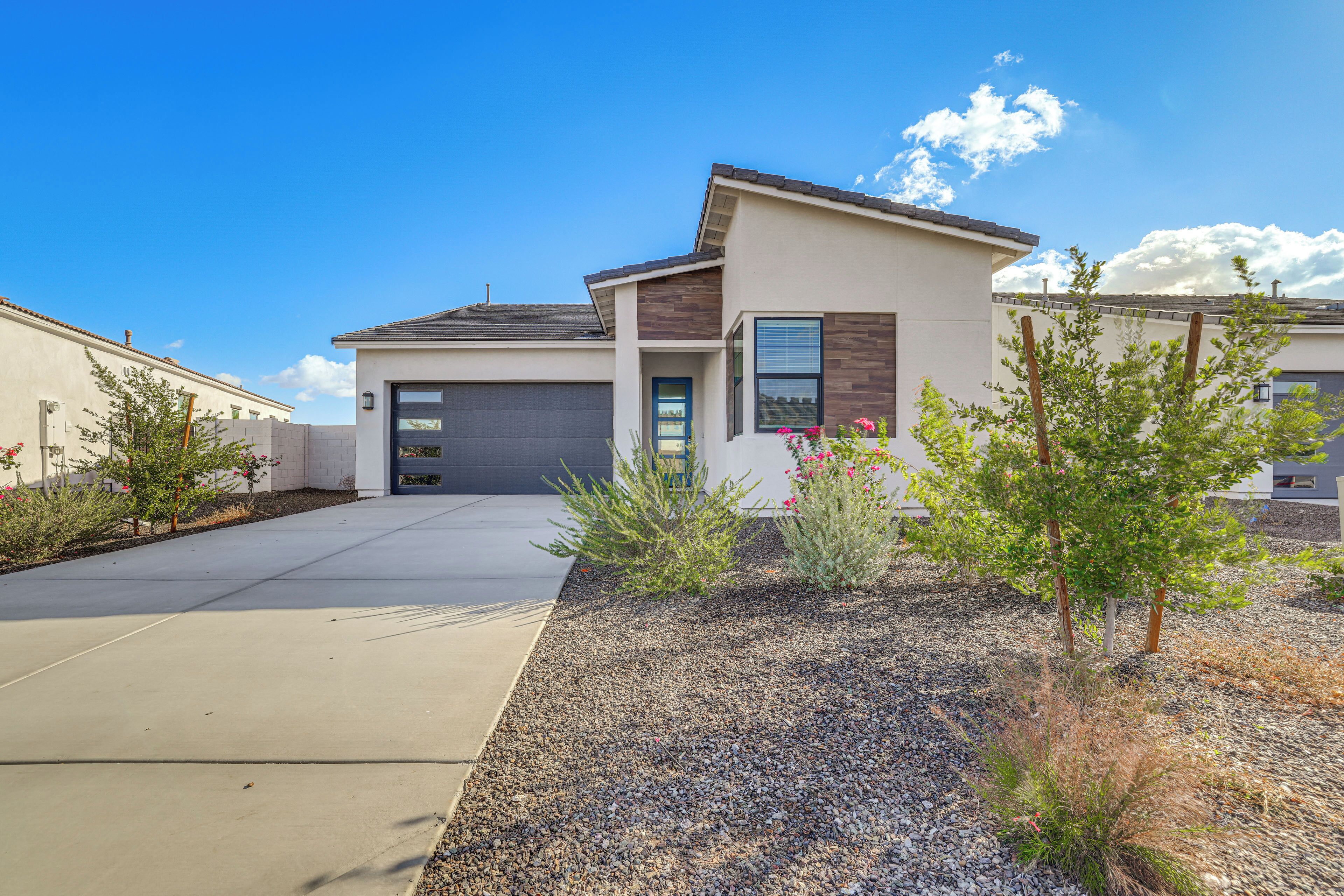 A modern single-story house with a garage, a driveway, and a landscaped garden with small trees and shrubs.