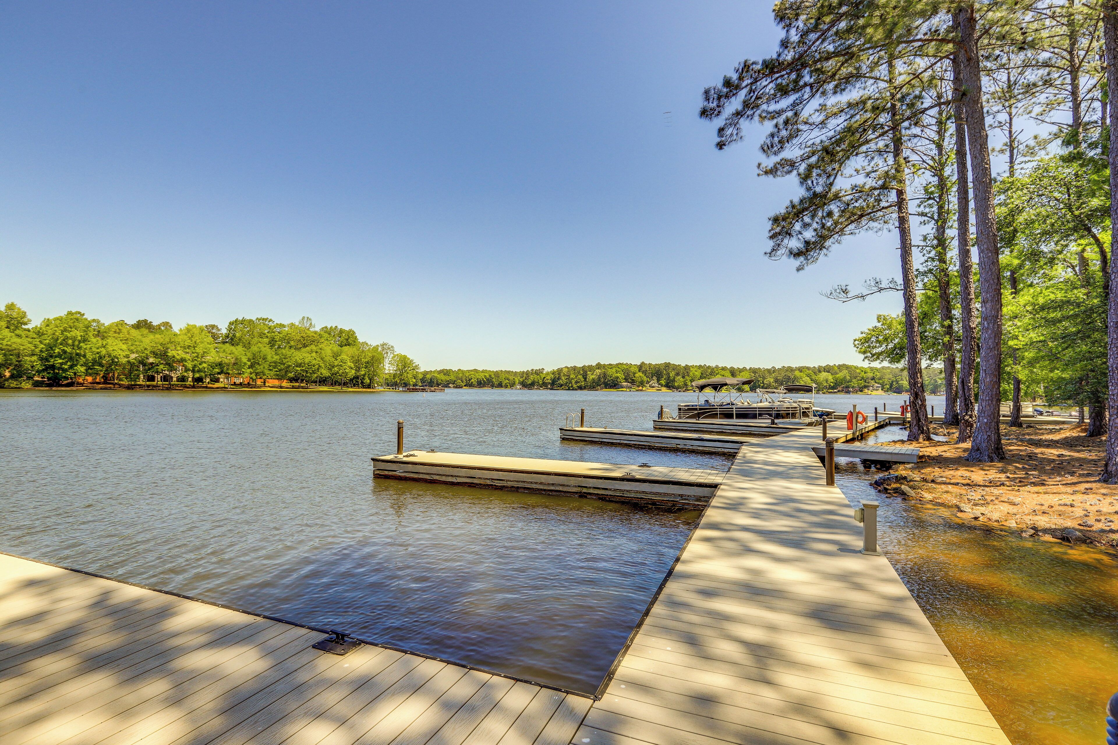 A wooden dock extending into a calm lake, surrounded by trees and a clear sky.