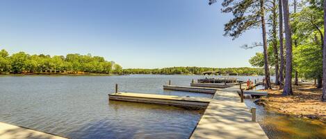 A wooden dock extending into a calm lake, surrounded by trees and a clear sky.
