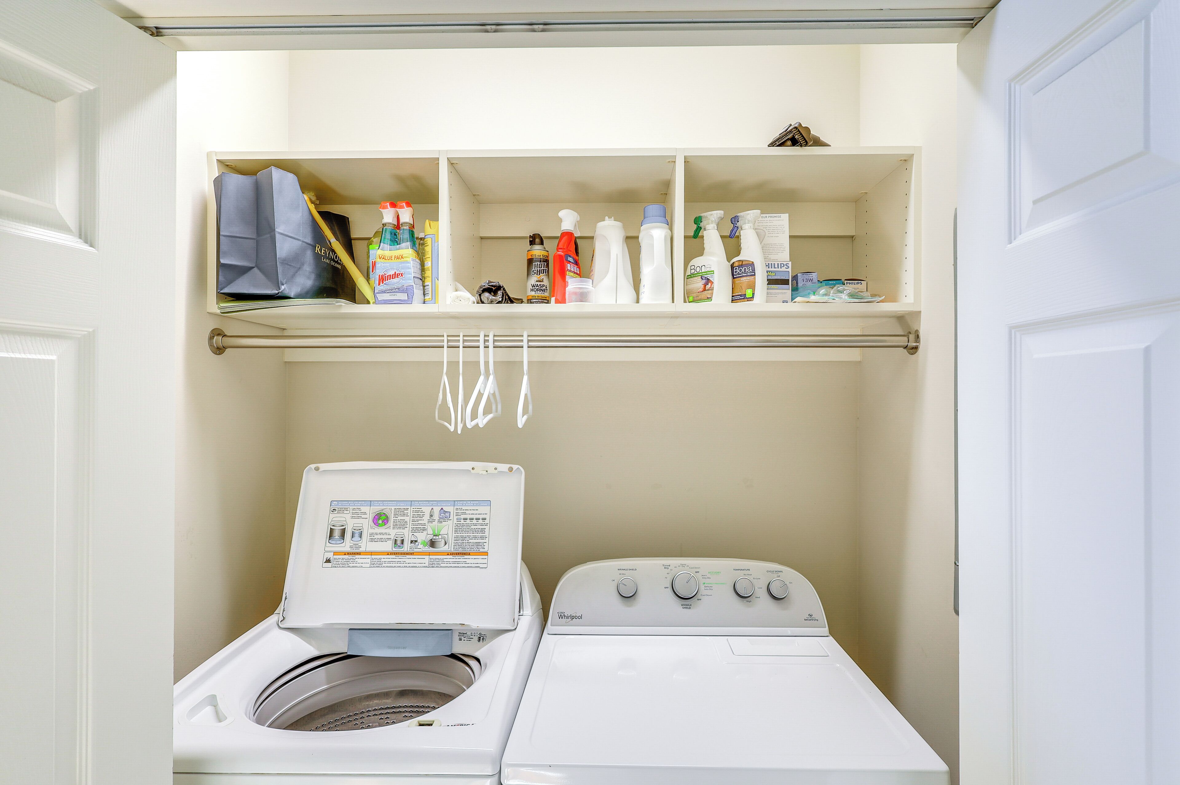 A laundry area with a washing machine and dryer, shelves with cleaning supplies, and a hanging rack.