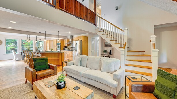 Amplia sala de estar con una escalera de madera, un sofá grande, una mesa de centro y una cocina al fondo.