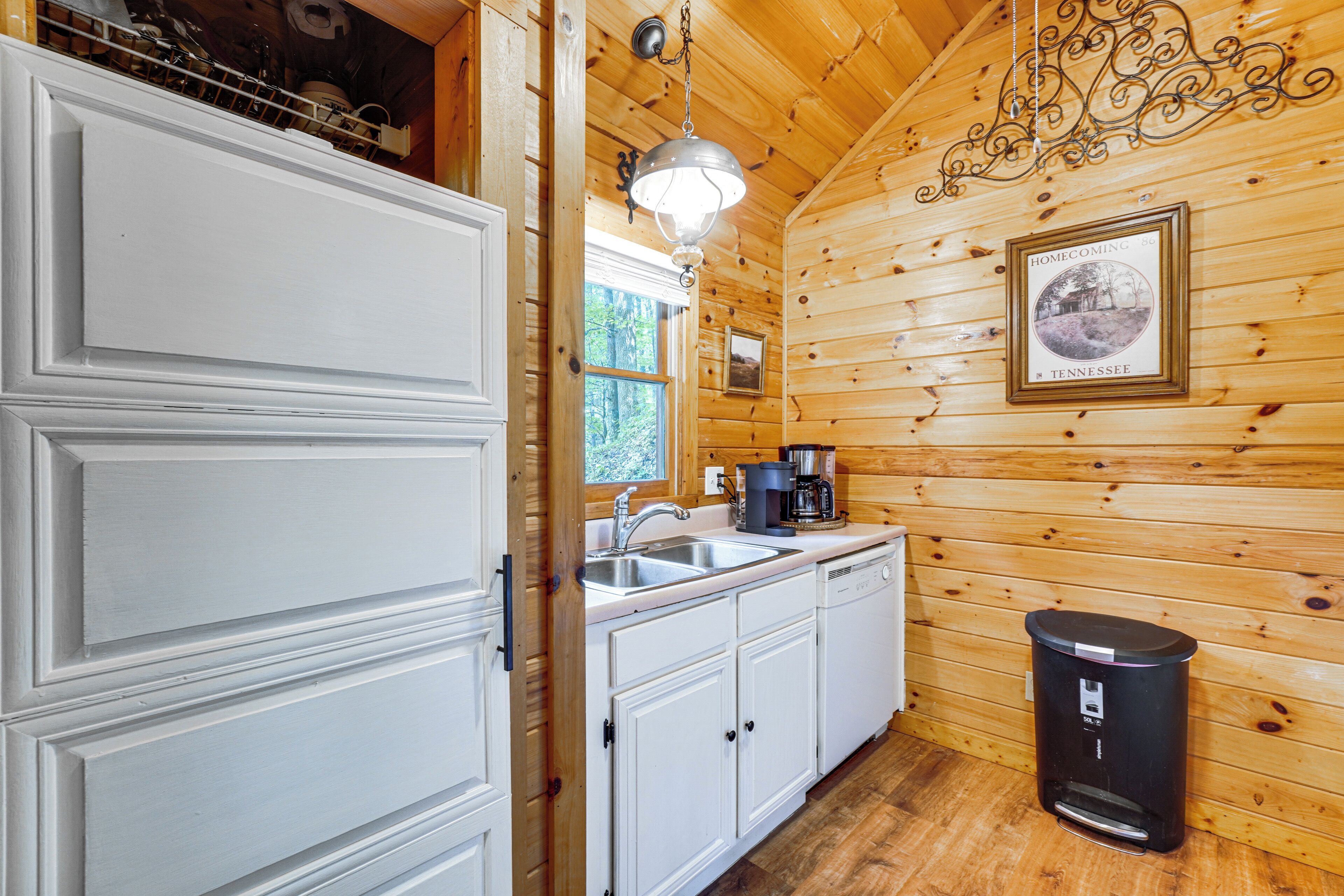 A kitchen with white cabinets, a sink, a coffee maker, and a trash can.