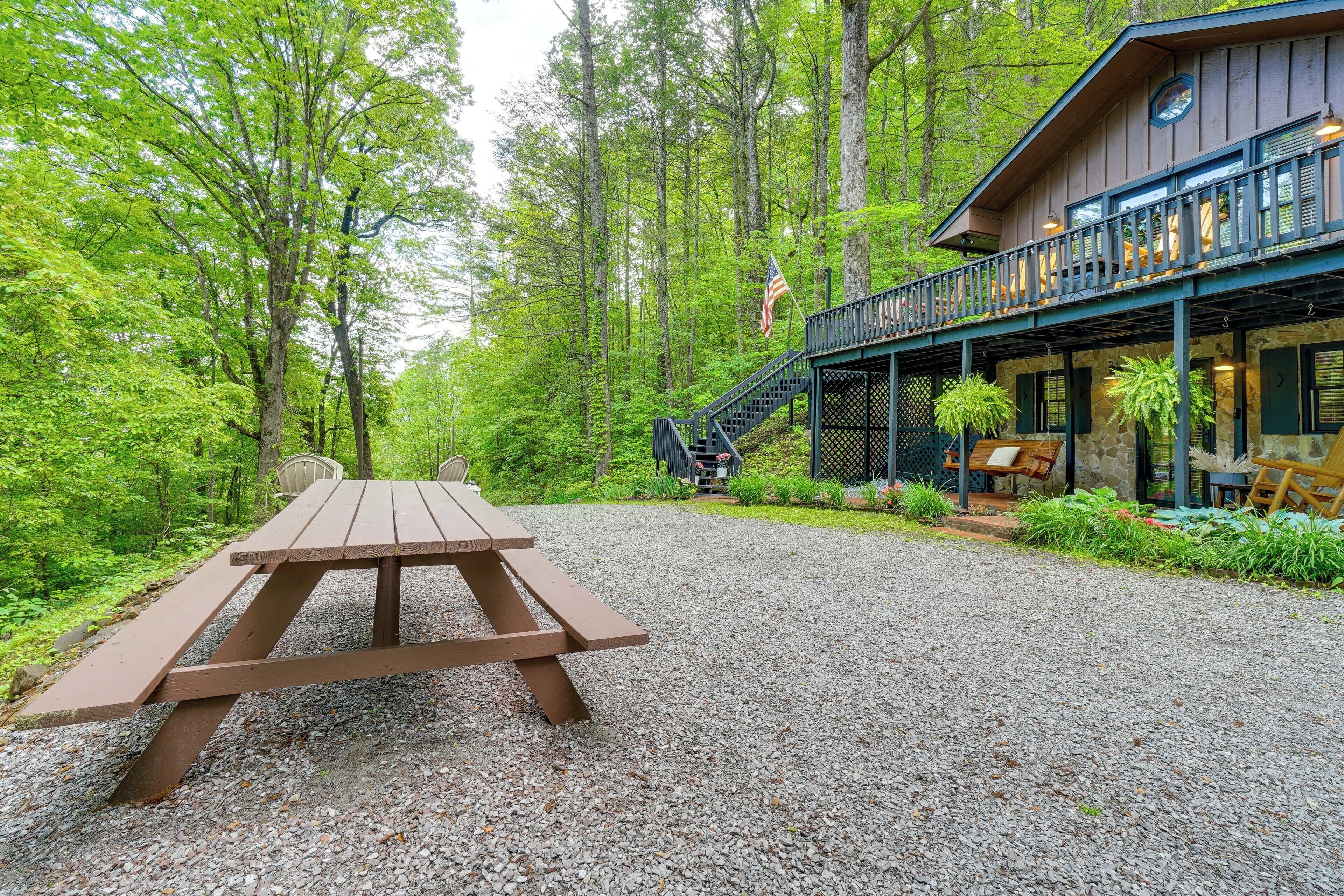 A wooden picnic table in a forested area with a building featuring a balcony and stairs.