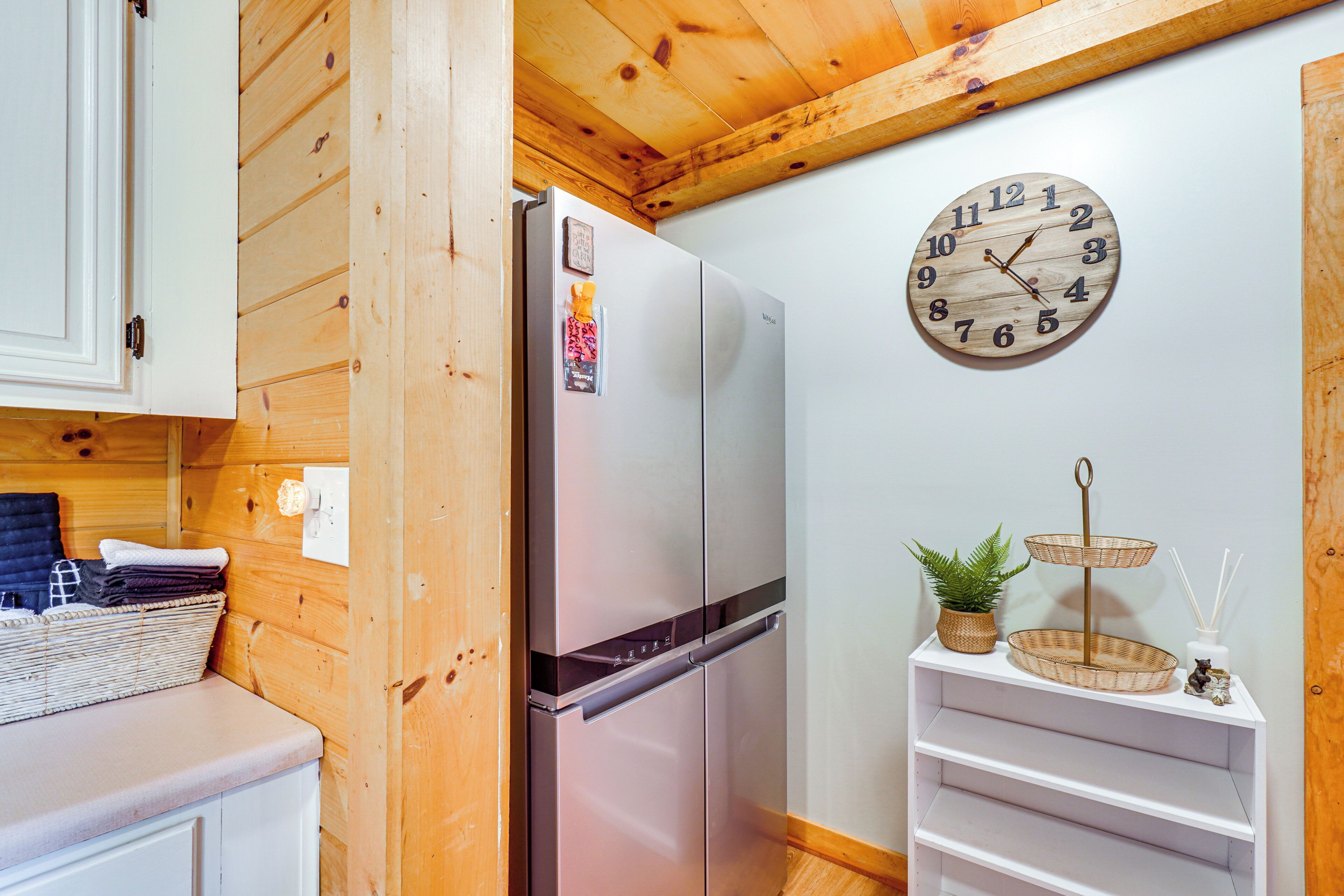 Una cocina compacta con refrigerador integrado, paredes de madera, un reloj de pared y un estante pequeño con adornos.