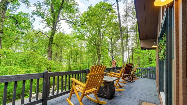 A wooden deck with rocking chairs and a table, overlooking a forested area. - 'bear Acres Getaway' Cabin w/ Deck in Townsend! (Townsend)