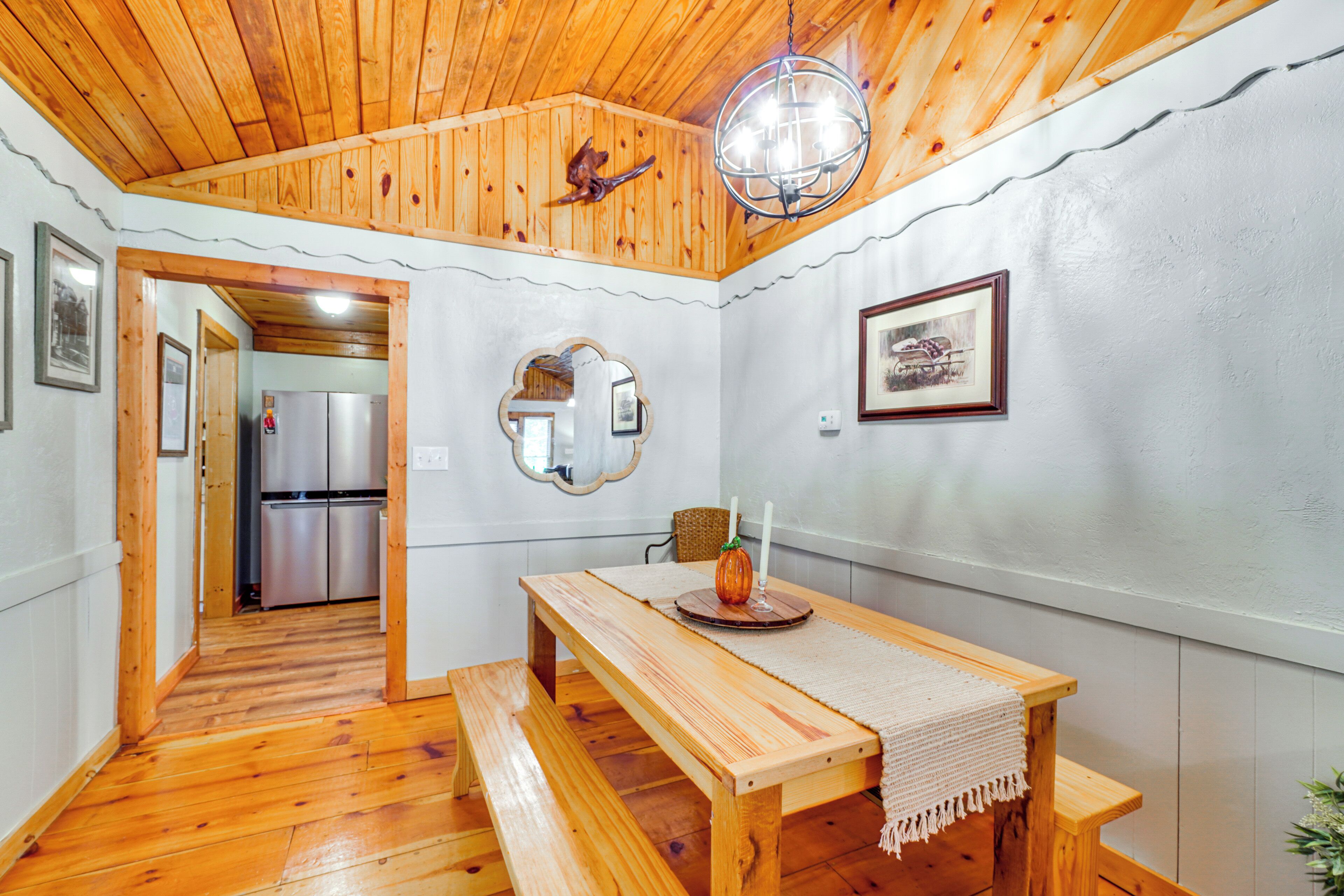 A wooden dining table with a bench, a chandelier, and a refrigerator in the background.