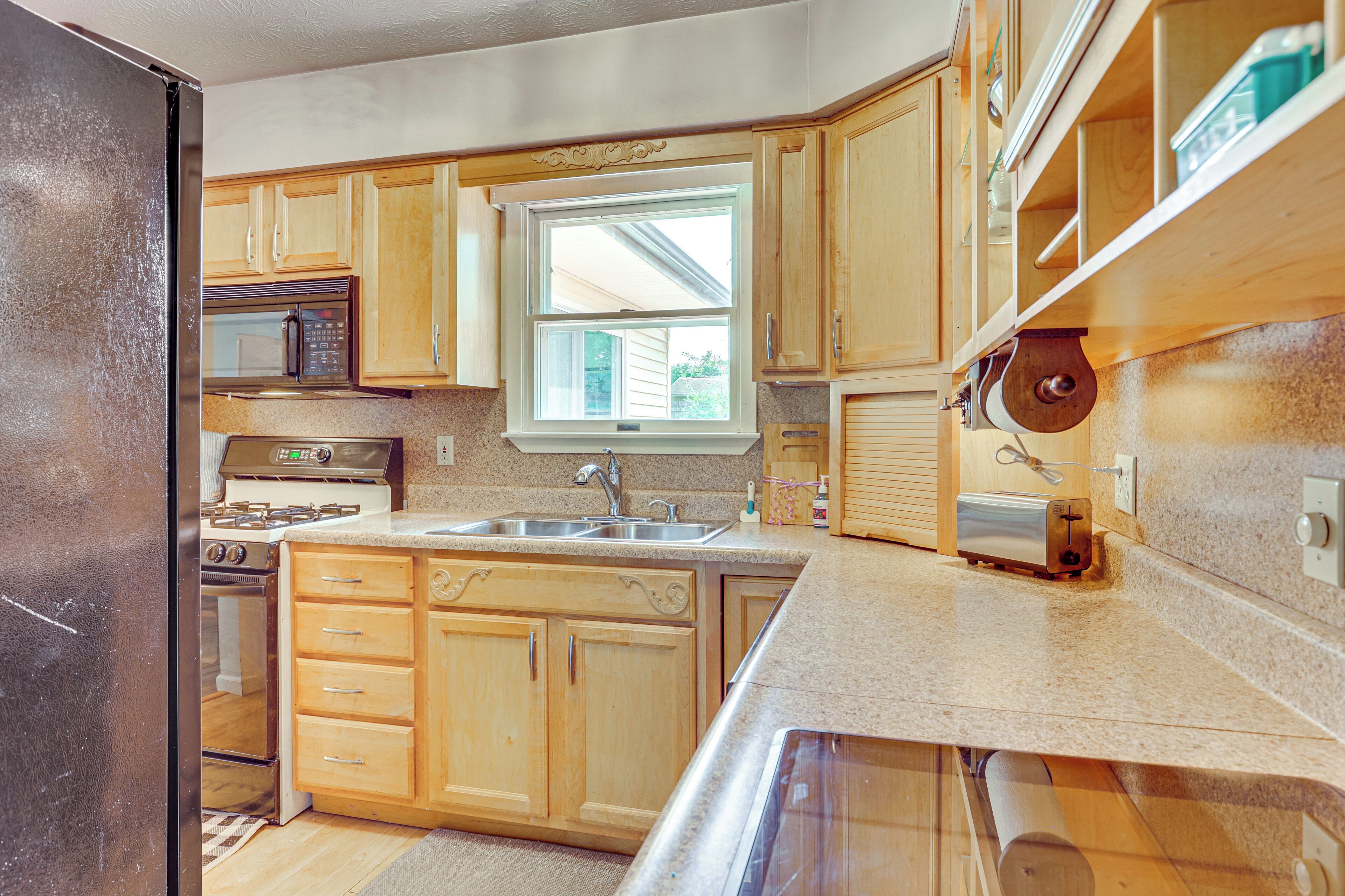 A kitchen with wooden cabinets, a microwave, a stove, a sink, and a window.