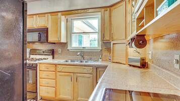 A kitchen with wooden cabinets, a microwave, a stove, a sink, and a window.