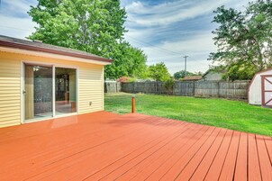 Una casa con terraza roja, puerta corredera de vidrio y patio trasero cercado.