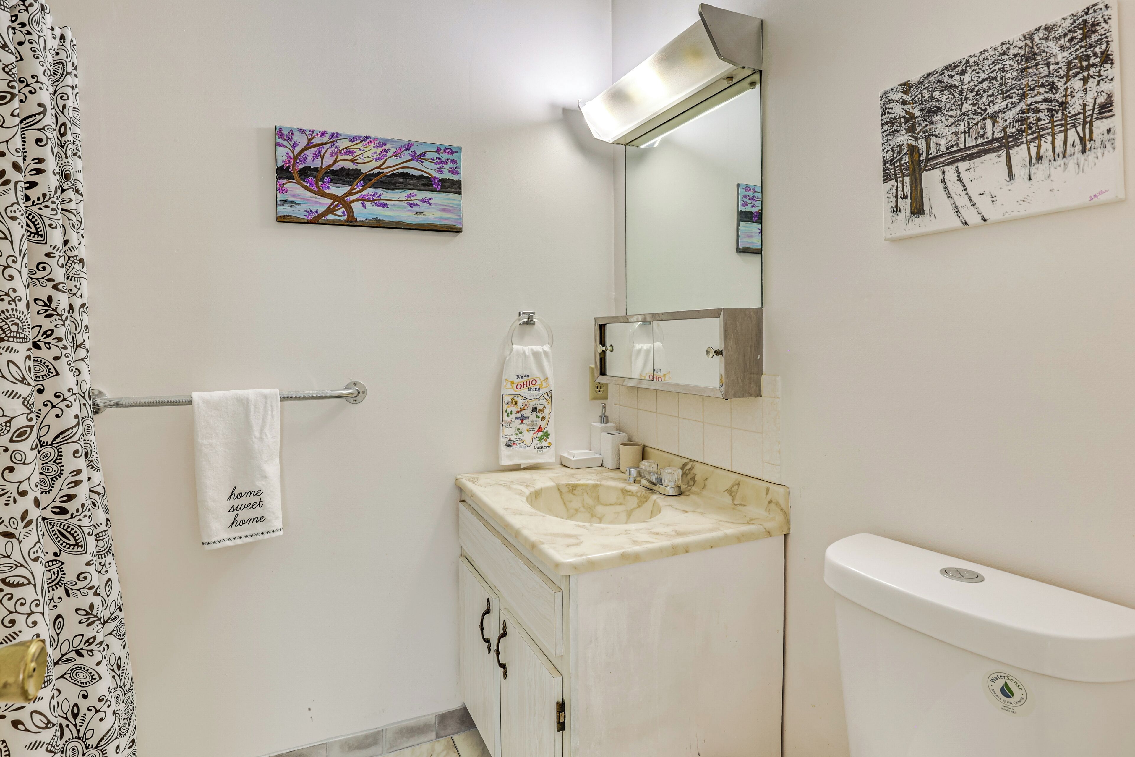 A bathroom with a marble sink, a toilet, a towel hanging on a rack, and two paintings on the walls.