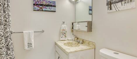 A bathroom with a marble sink, a toilet, a towel hanging on a rack, and two paintings on the walls.