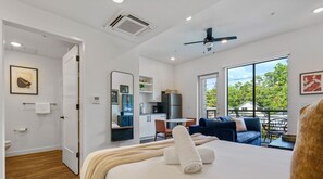 A modern hotel room with a bed, a seating area with a sofa and chairs, a kitchenette, and a balcony with a view of the outdoors. - Vibrant Austin Studio | Balcony + Parking + Wi-Fi (Austin)
