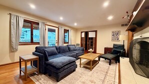 Un salón con sofá, una mesa de centro, chimenea y vistas al exterior.