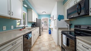 Una cocina con armarios blancos, un microondas negro y un refrigerador de acero inoxidable.