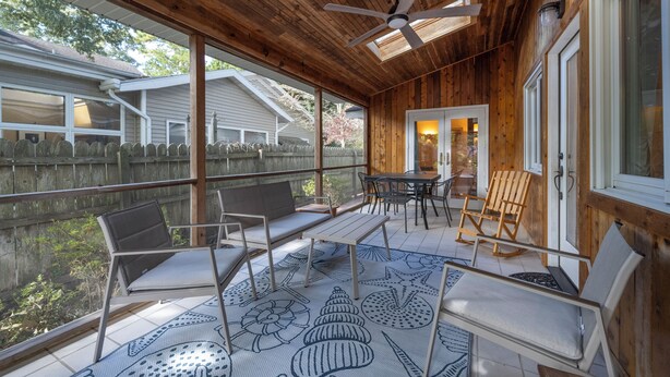 Un patio exterior techado con piso de madera, un ventilador de techo y un comedor con sillas y una mesa.