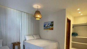 A bedroom with a bed, a small wooden nightstand, a painting of a sailboat, and a built-in shelving unit. - Casa nobre Trancoso  (Porto Seguro)