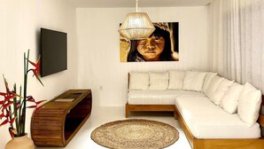 A modern living room with a sectional sofa, a wooden console table, a round woven rug, a tall floor lamp, and a large framed artwork on the wall. - Casa nobre Trancoso  (Porto Seguro)