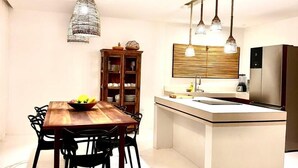 A modern kitchen with a central island, pendant lighting, and a dining area with a wooden table and chairs. - Casa nobre Trancoso  (Porto Seguro)