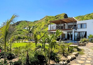 A modern two-story house with a balcony, surrounded by lush greenery and a rocky landscape. - HOP KAI Hermosa Casa de Playa en Punta Sal (Canoas de Punta Sal)